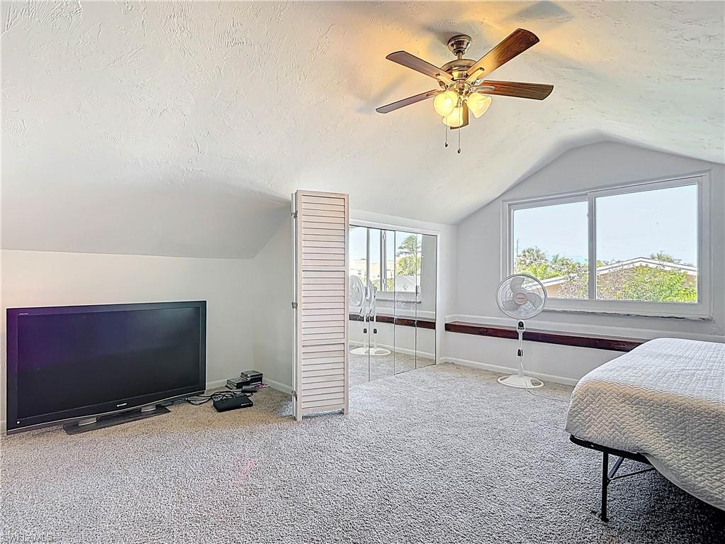 Bedroom featuring a textured ceiling, vaulted ceiling, a ceiling fan, and light colored carpet