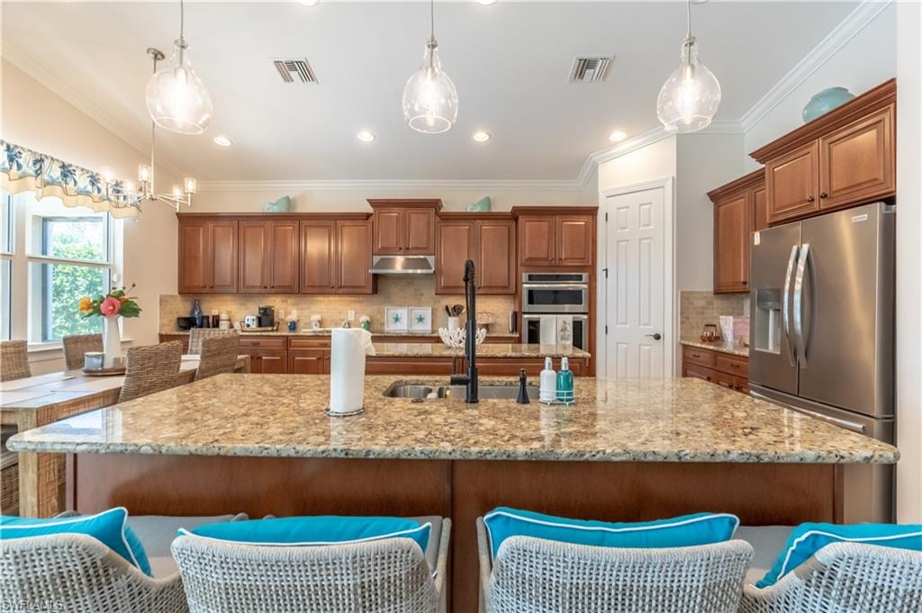 Kitchen with brown cabinetry, stainless steel appliances, pendant lighting, crown molding, and a breakfast bar