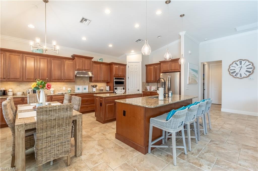 Kitchen featuring brown cabinetry, a breakfast bar area, crown molding, pendant lighting, and tasteful backsplash