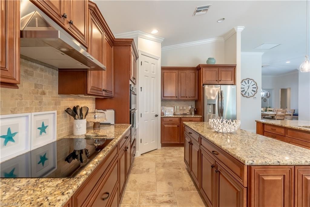 Kitchen with brown cabinets, under cabinet range hood, decorative backsplash, ornamental molding, and black electric cooktop