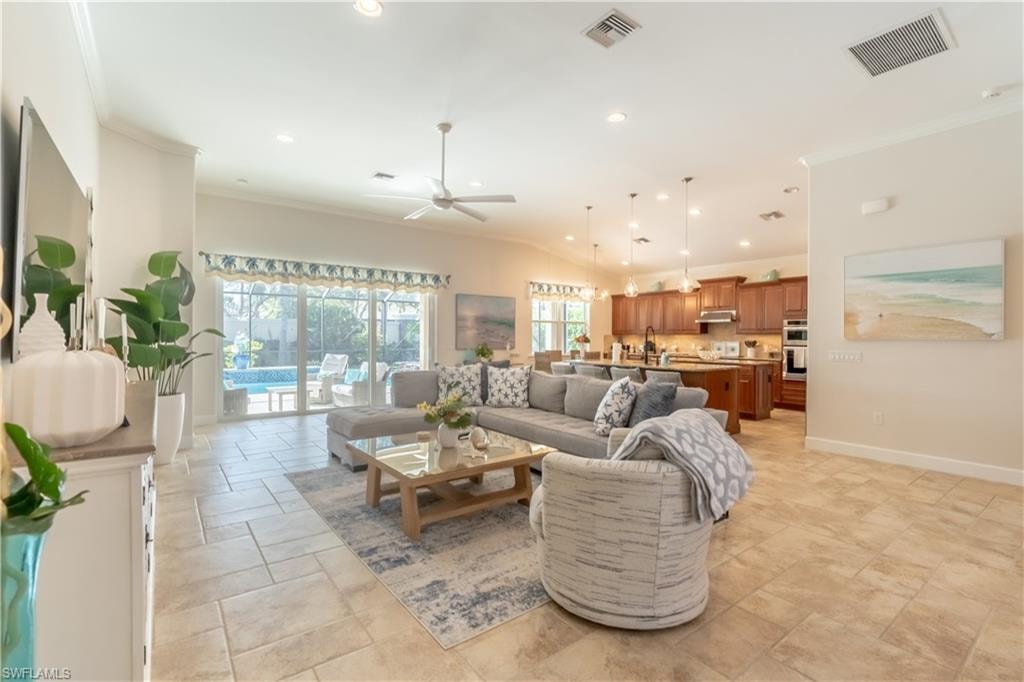 Living room with ornamental molding, recessed lighting, ceiling fan, and stone tile floors
