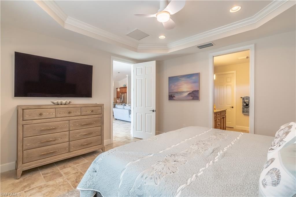 Bedroom with ornamental molding, a ceiling fan, connected bathroom, a tray ceiling, and recessed lighting