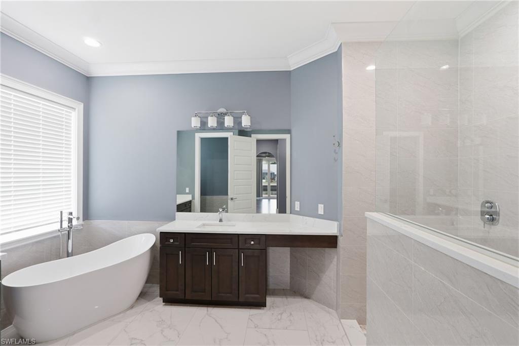 Full bathroom featuring a freestanding bath, vanity, ornamental molding, a walk in shower, and light marble finish floors
