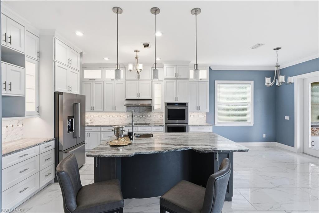 Kitchen with a chandelier, light stone counters, decorative light fixtures, white cabinets, and crown molding