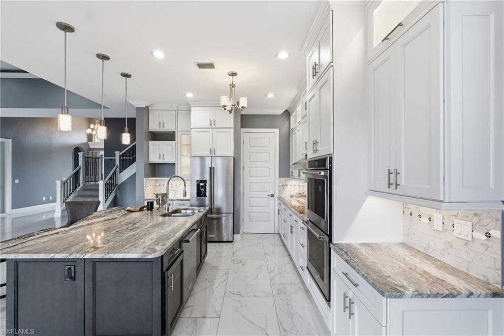 Kitchen featuring decorative backsplash, a chandelier, white cabinetry, pendant lighting, and stainless steel appliances