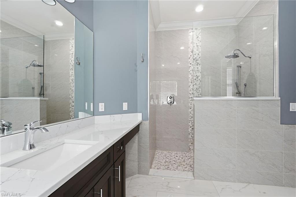 Bathroom featuring a walk in shower, vanity, light marble finish floors, crown molding, and recessed lighting