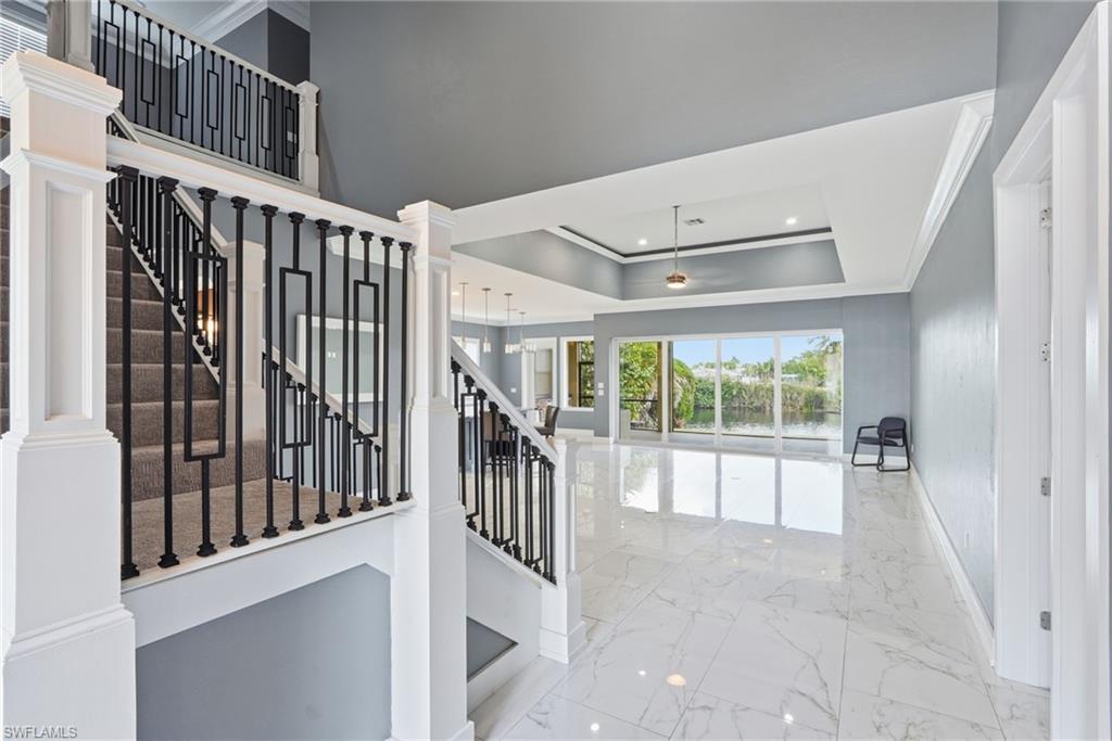 Staircase with marble tiled floors, ornamental molding, recessed lighting, a raised ceiling, and decorative columns