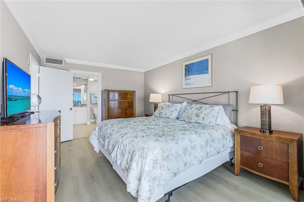 Bedroom with light wood finished floors, ornamental molding, and ensuite bathroom