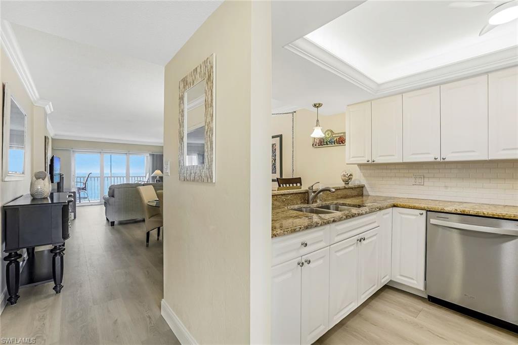Kitchen featuring dark stone countertops, ornamental molding, light wood finished floors, dishwasher, and backsplash