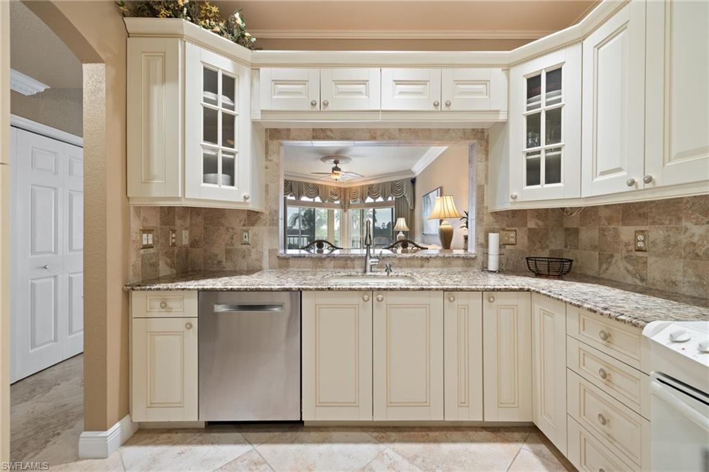 Kitchen featuring cream cabinetry, glass insert cabinets, ornamental molding, light stone countertops, and backsplash
