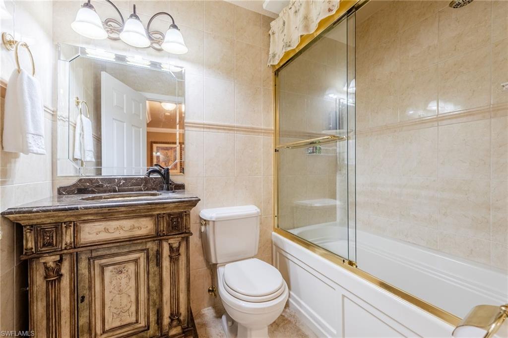 Full bathroom featuring tile walls, vanity, and bath / shower combo with glass door