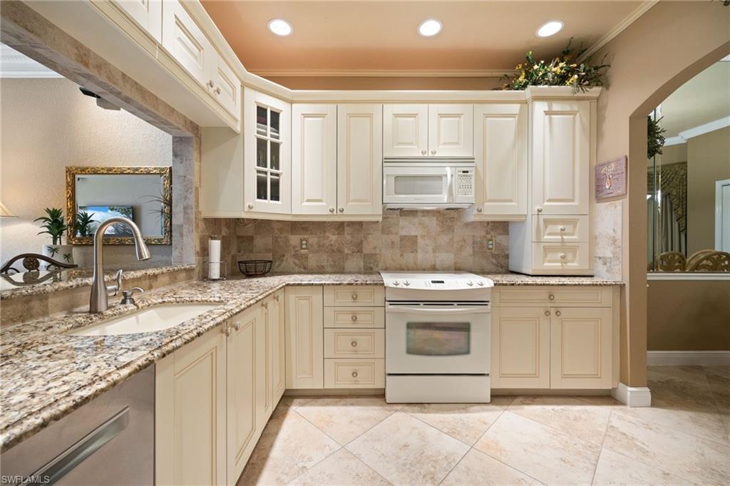 Kitchen featuring cream cabinetry, white appliances, arched walkways, light stone counters, and ornamental molding
