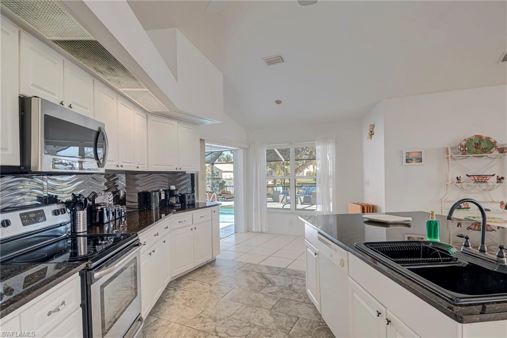 Kitchen with appliances with stainless steel finishes, white cabinets, dark stone counters, and decorative backsplash