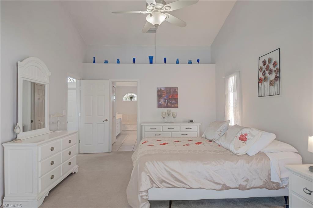 Bedroom with high vaulted ceiling, carpet floors, multiple windows, a ceiling fan, and ensuite bathroom