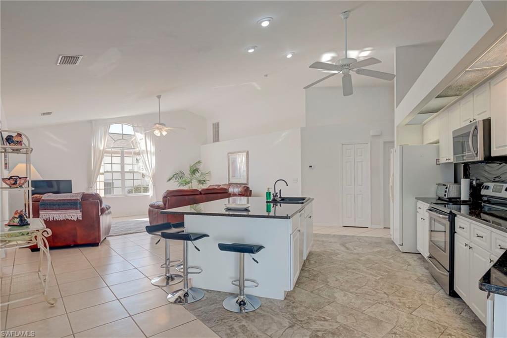 Kitchen with white cabinets, appliances with stainless steel finishes, open floor plan, a center island with sink, and a kitchen bar