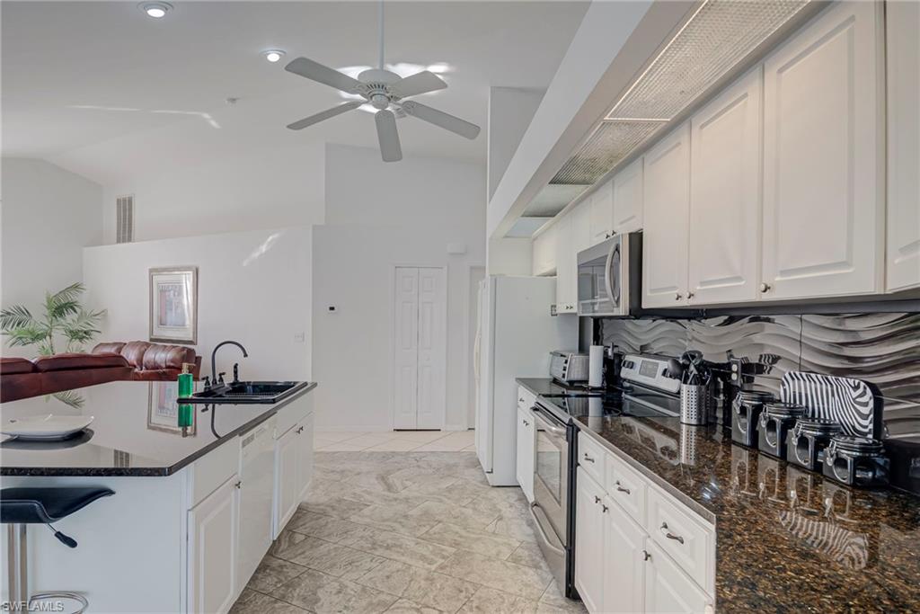 Kitchen featuring open floor plan, stainless steel appliances, dark stone counters, white cabinets, and vaulted ceiling