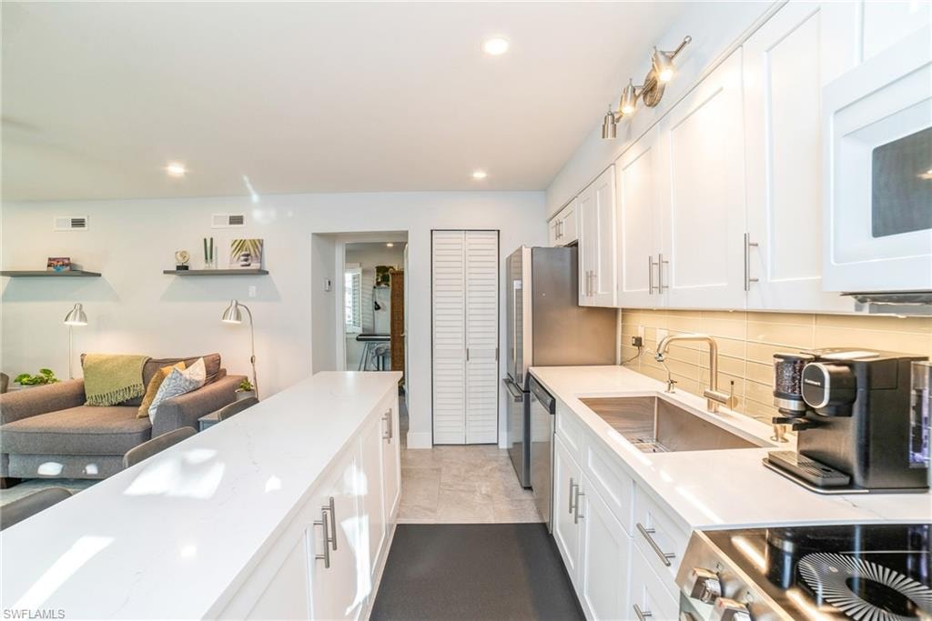 Kitchen with white cabinets, appliances with stainless steel finishes, light stone counters, decorative backsplash, and open floor plan