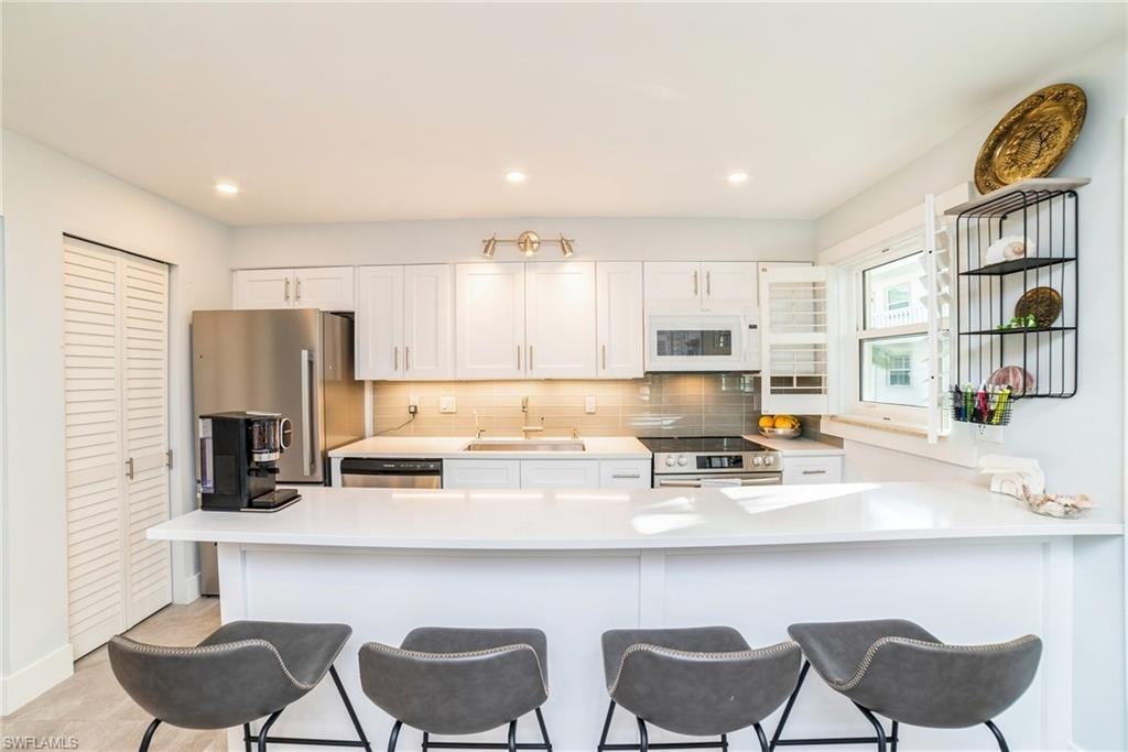 Kitchen with white cabinets, a peninsula, stainless steel appliances, backsplash, and recessed lighting