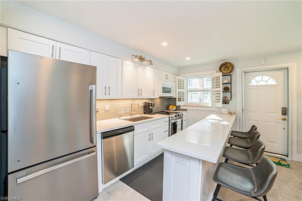 Kitchen with appliances with stainless steel finishes, white cabinets, a breakfast bar area, backsplash, and a peninsula