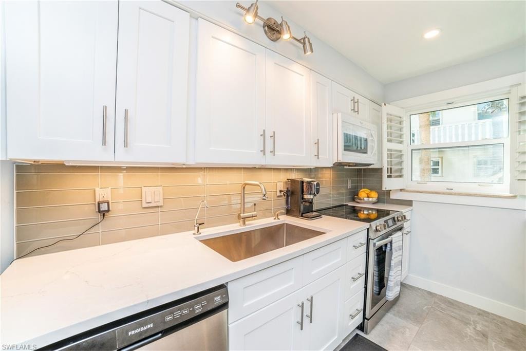 Kitchen with white cabinets, appliances with stainless steel finishes, tasteful backsplash, and light stone counters