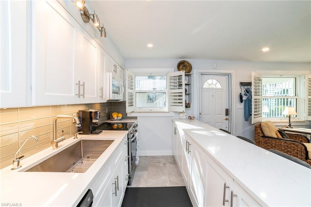 Kitchen featuring white cabinets, backsplash, stainless steel electric stove, light stone counters, and white microwave