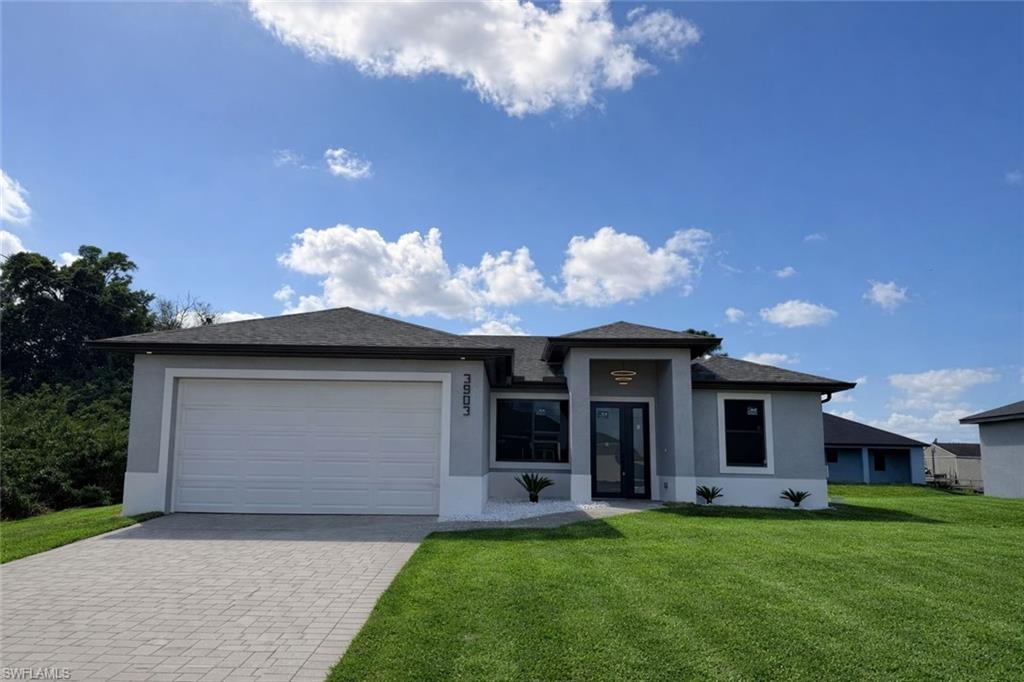 Prairie-style home featuring a front yard, a garage, decorative driveway, and stucco siding