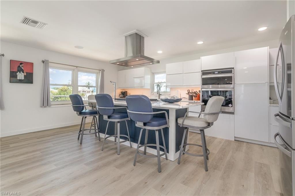 Kitchen with modern cabinets, white cabinetry, appliances with stainless steel finishes, a breakfast bar area, and a center island