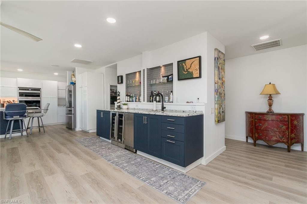 Bar area featuring blue cabinets, white cabinets, stainless steel appliances, light wood-type flooring, and light stone countertops