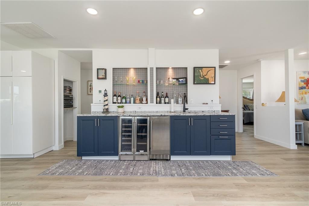 Indoor wet bar featuring blue cabinets, beverage cooler, light stone countertops, light wood-style floors, and recessed lighting