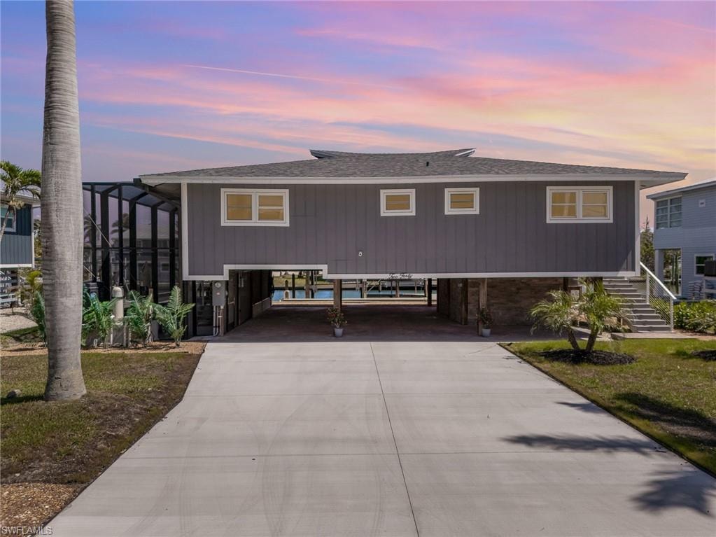 View of front of house with a carport, a shingled roof, stairs, and driveway