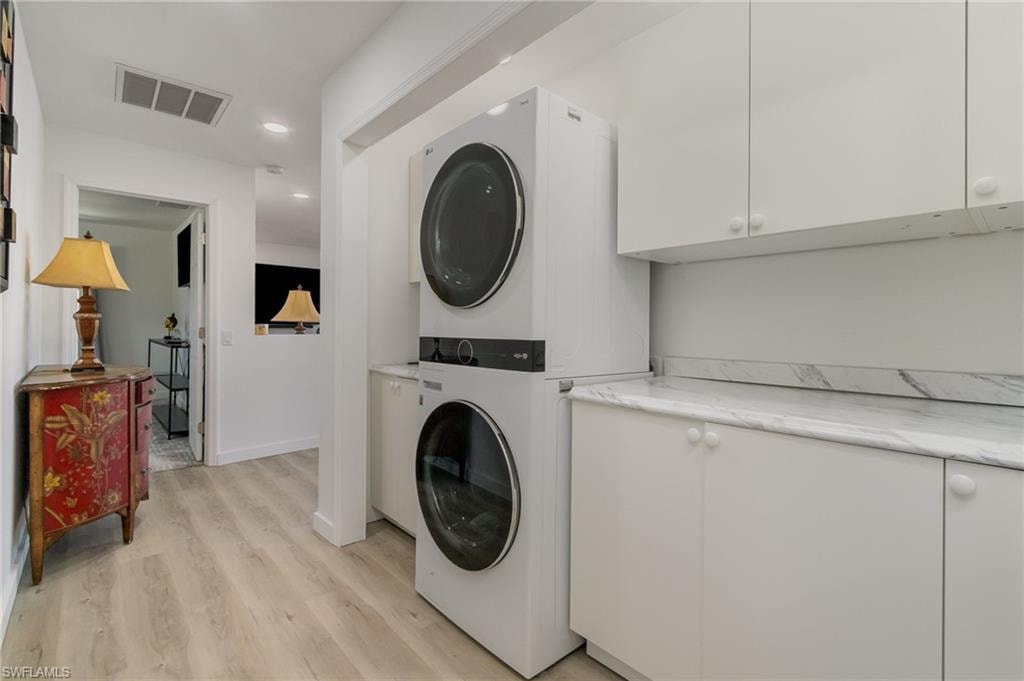 Washroom with stacked washer / dryer, light wood-style flooring, recessed lighting, and cabinet space