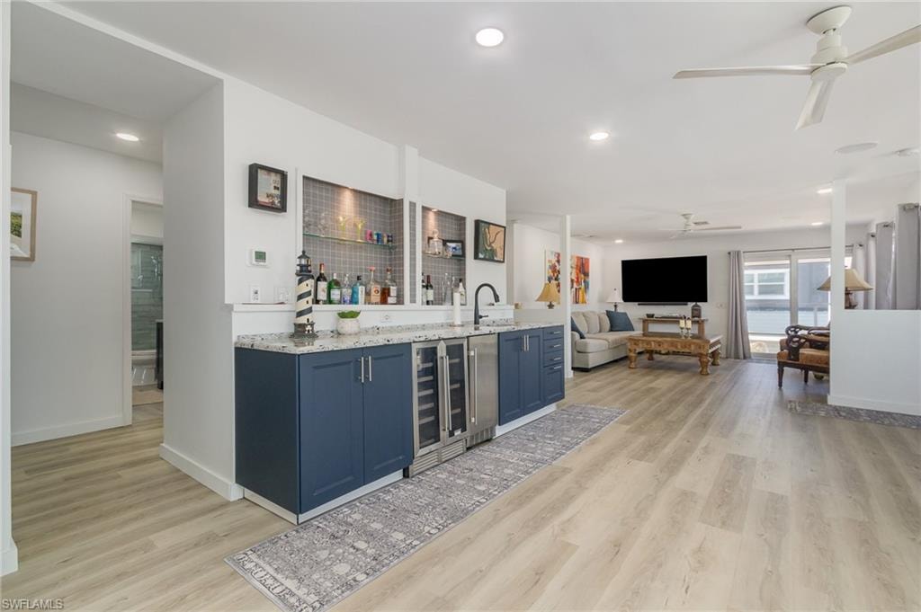 Indoor wet bar with light stone countertops, blue cabinets, light wood-style floors, recessed lighting, and beverage cooler