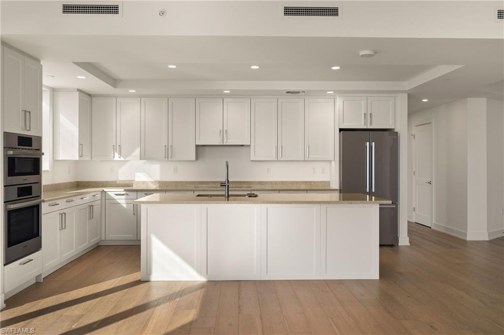 Kitchen with recessed lighting, appliances with stainless steel finishes, white cabinets, light stone countertops, and light wood finished floors