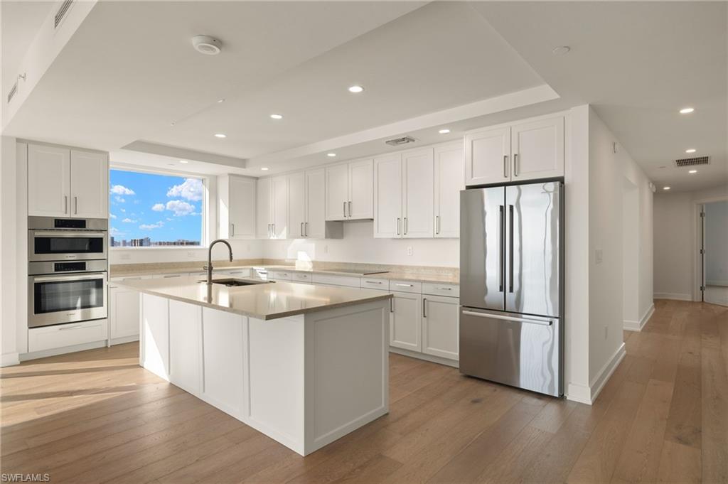 Spacious kitchen featuring appliances with stainless steel finishes, white cabinetry, recessed lighting, a tray ceiling, and light wood-style floors