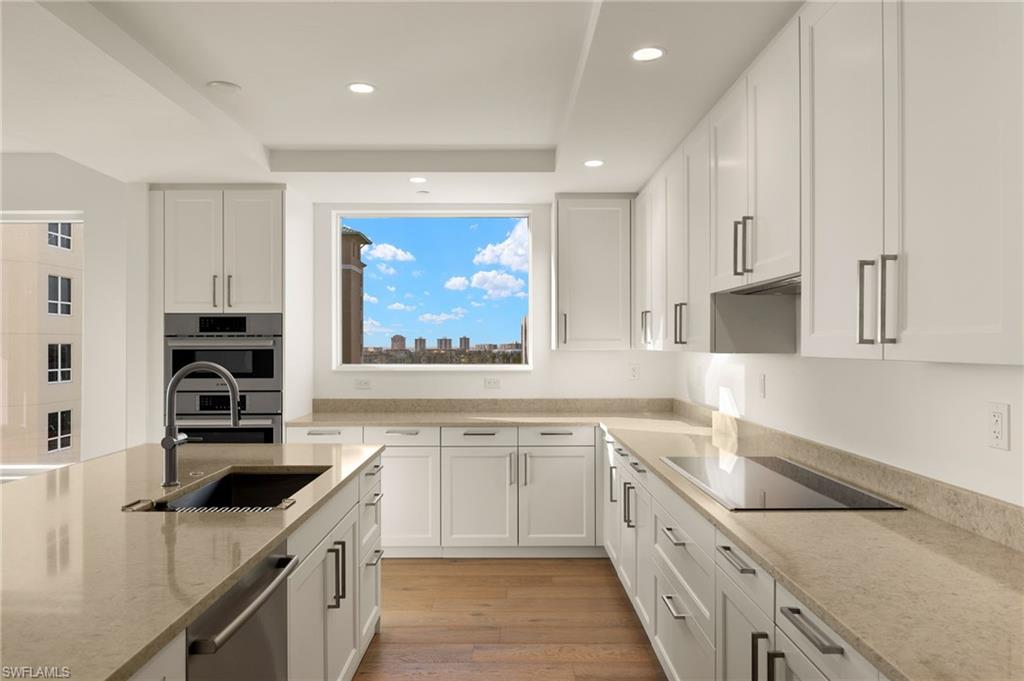 Lots of cabinets in this light and airy Kitchen featuring light stone counters, white cabinetry, light wood-style floors, stainless steel appliances, and a raised ceiling