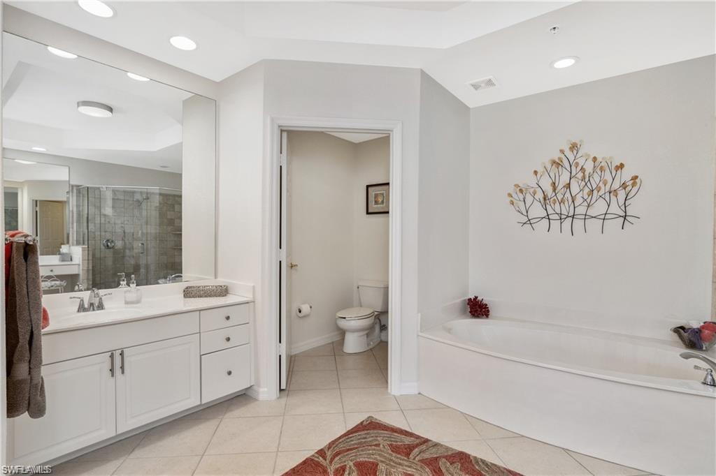 Full bathroom with vanity, a shower stall, recessed lighting, a tray ceiling, and a bath