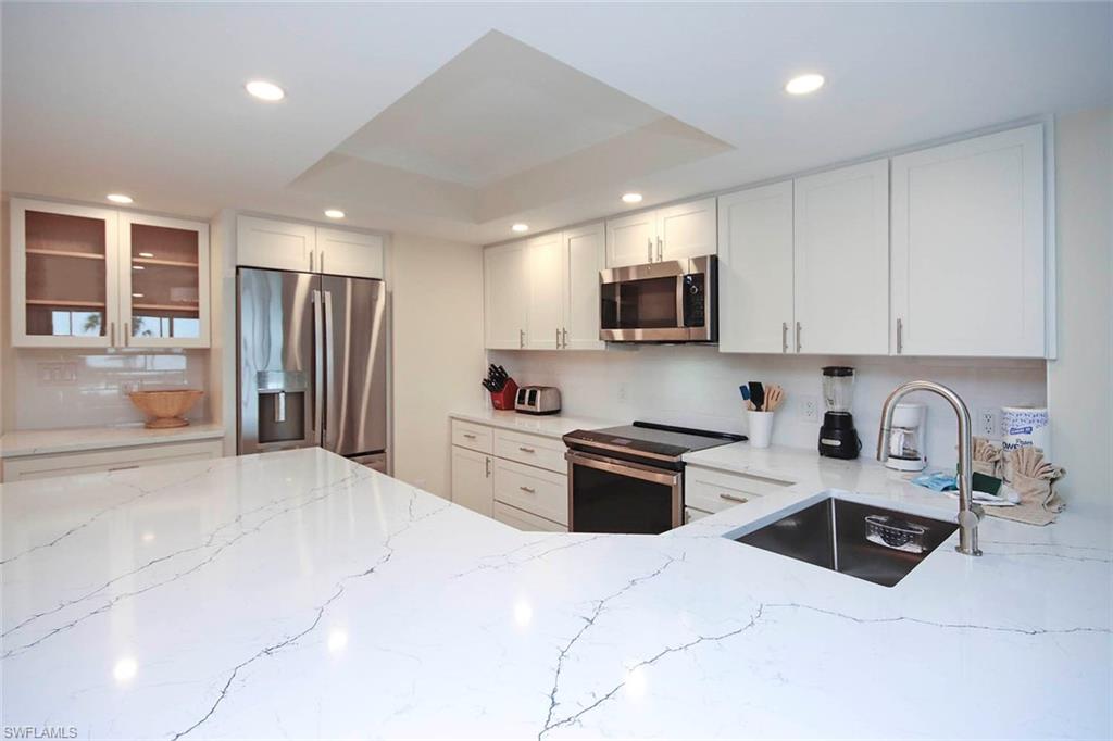 Kitchen featuring light stone counters, stainless steel appliances, white cabinetry, a raised ceiling, and glass insert cabinets