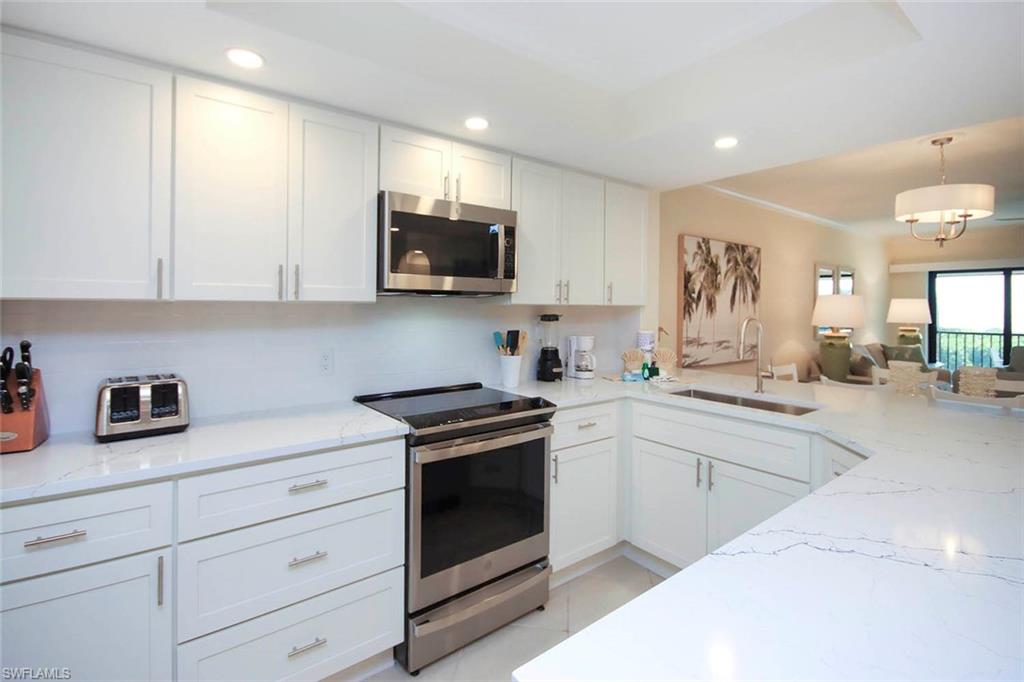 Kitchen featuring stainless steel appliances, white cabinetry, light stone counters, hanging light fixtures, and recessed lighting