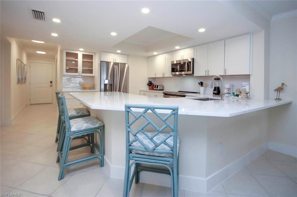 Kitchen featuring a kitchen breakfast bar, a peninsula, light stone counters, stainless steel appliances, and white cabinetry
