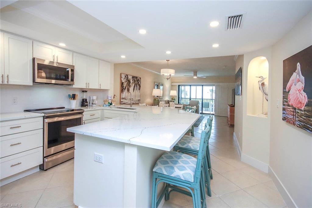 Kitchen featuring appliances with stainless steel finishes, a breakfast bar, light tile patterned floors, white cabinetry, and light stone counters