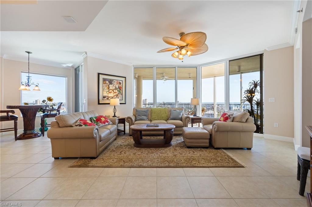 Living room with a wall of windows, crown molding, healthy amount of natural light, a ceiling fan, and light tile patterned flooring