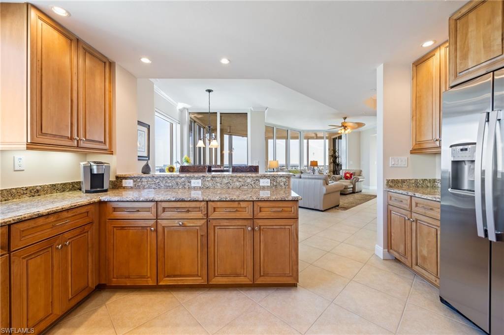 Kitchen with light stone countertops, stainless steel refrigerator with ice dispenser, recessed lighting, brown cabinets, and a peninsula