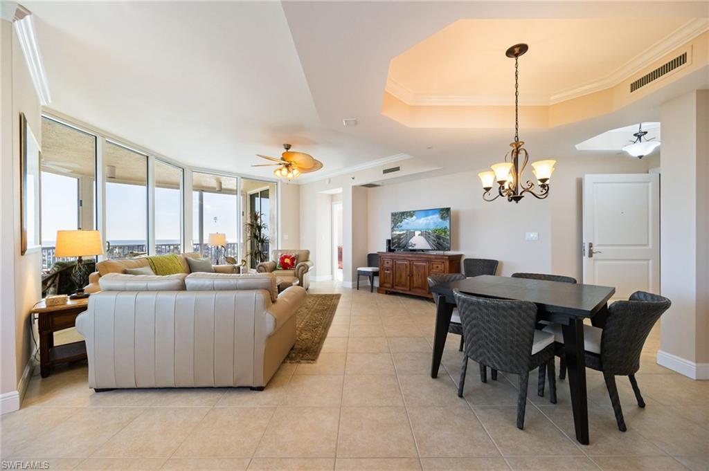 Living room with ornamental molding, a ceiling fan, a chandelier, floor to ceiling windows, and light tile patterned floors