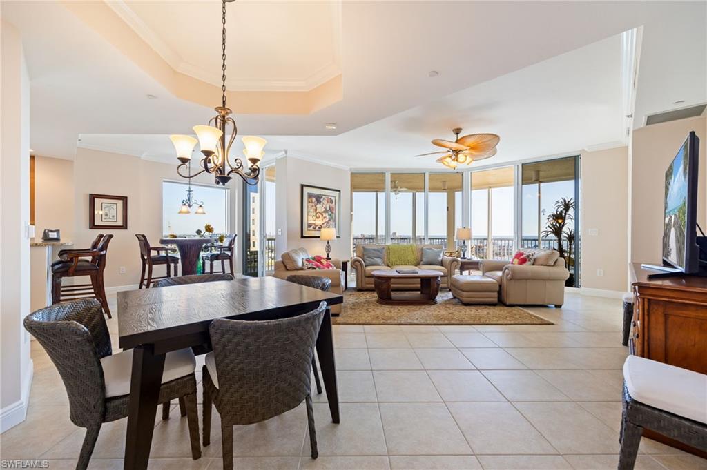 Dining room with crown molding, light tile patterned floors, a wall of windows, ceiling fan, and a raised ceiling