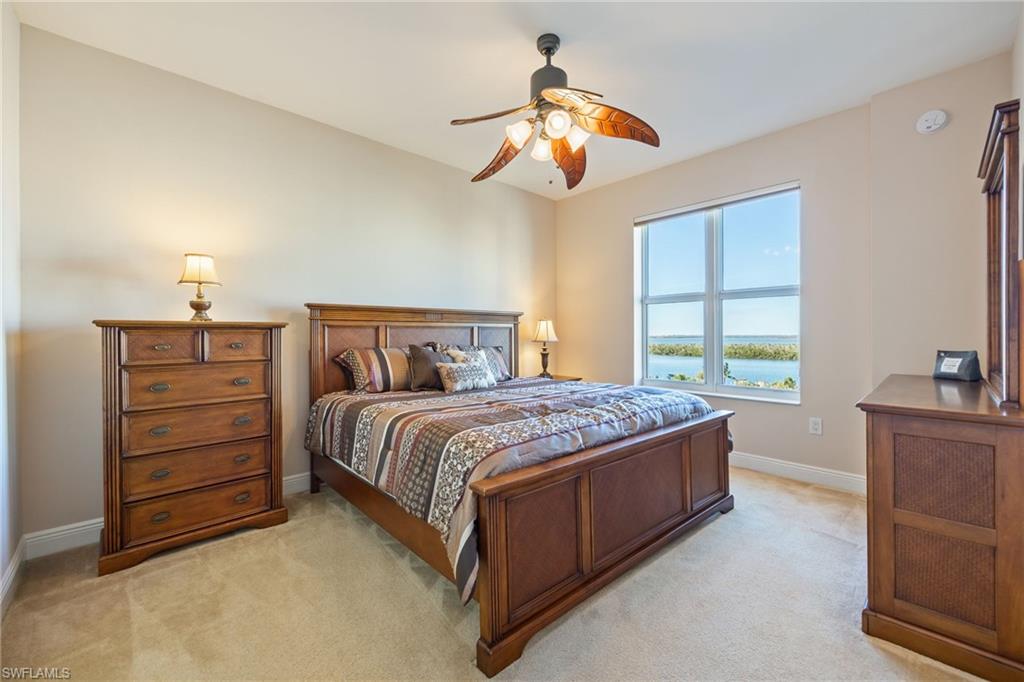 Bedroom with light colored carpet, ceiling fan, and a water view