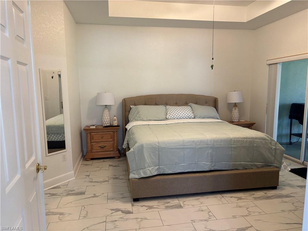 Bedroom with marble look tile flooring, a tray ceiling, and access to exterior