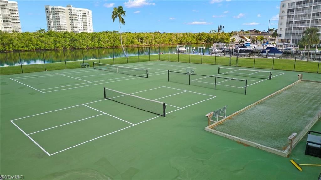View of tennis court with community basketball court and a water view