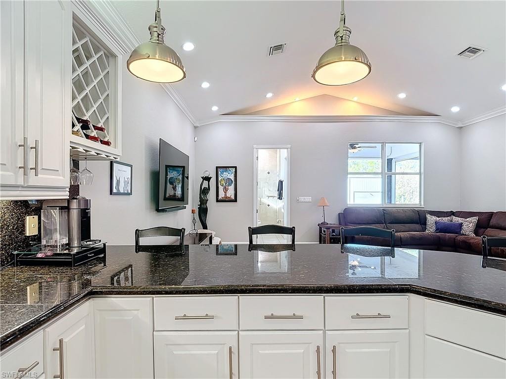Kitchen with open floor plan, dark stone counters, ornamental molding, white cabinetry, and lofted ceiling