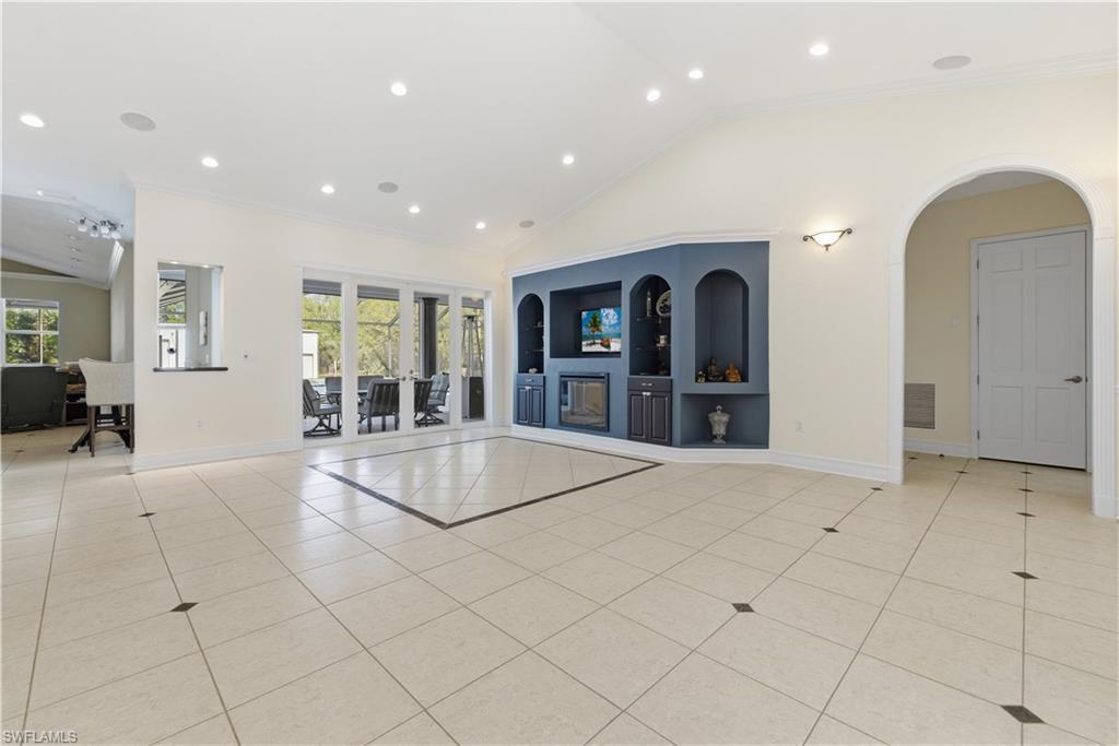Unfurnished living room featuring lofted ceiling, built in shelves, light tile patterned floors, recessed lighting, and ornamental molding