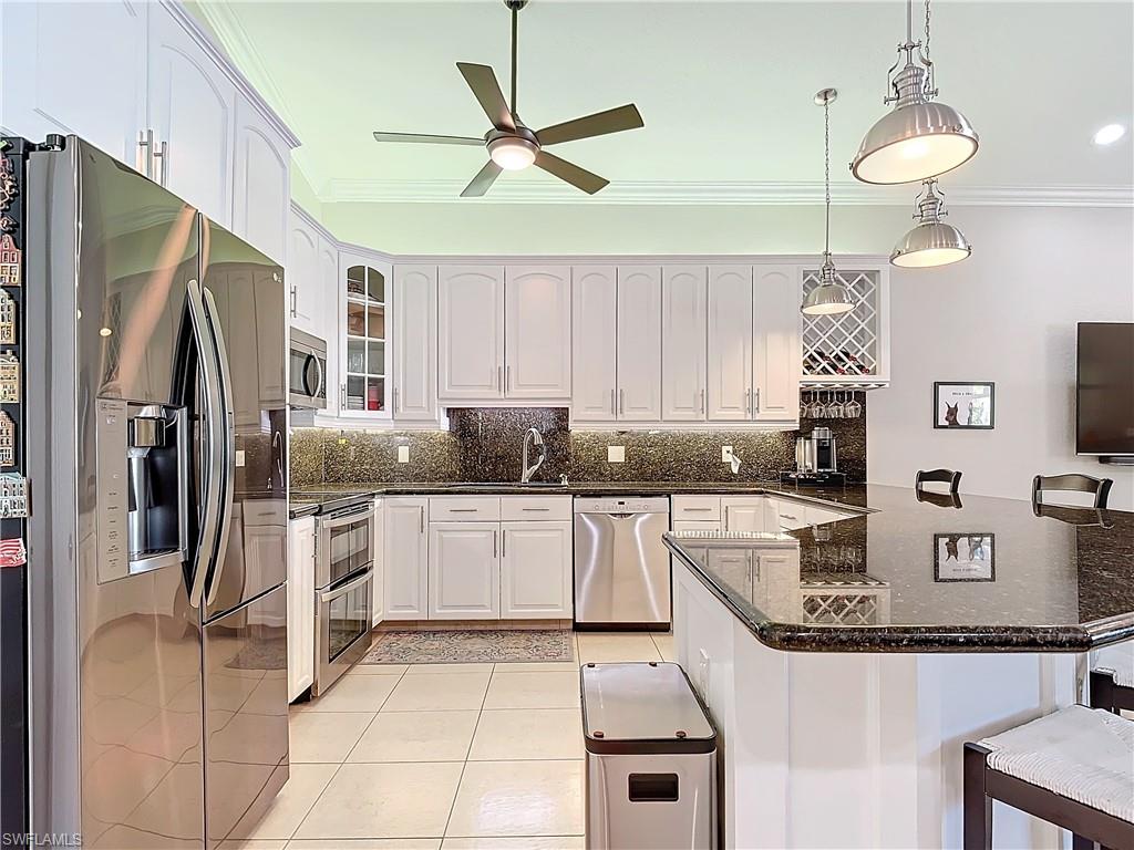 Kitchen featuring a kitchen breakfast bar, appliances with stainless steel finishes, dark stone counters, white cabinetry, and decorative light fixtures